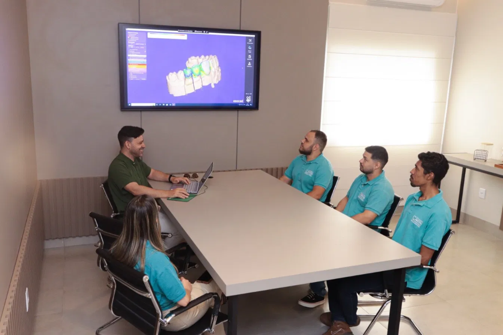 Equipe Odonto Prótese em reunião com software CAD na TV