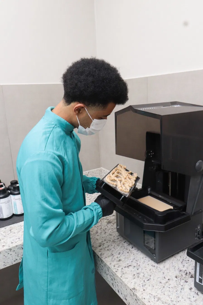Técnico retirando plataforma de impressão 3D com próteses